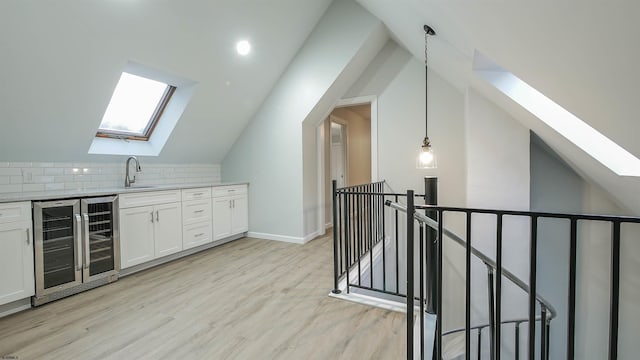 interior space with sink, white cabinetry, light hardwood / wood-style floors, decorative light fixtures, and beverage cooler