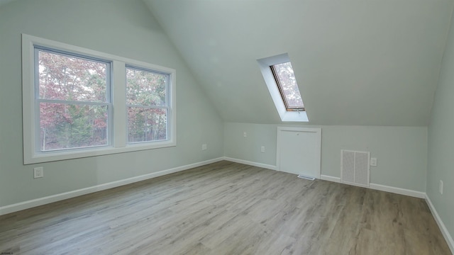 bonus room with vaulted ceiling with skylight and light wood-type flooring