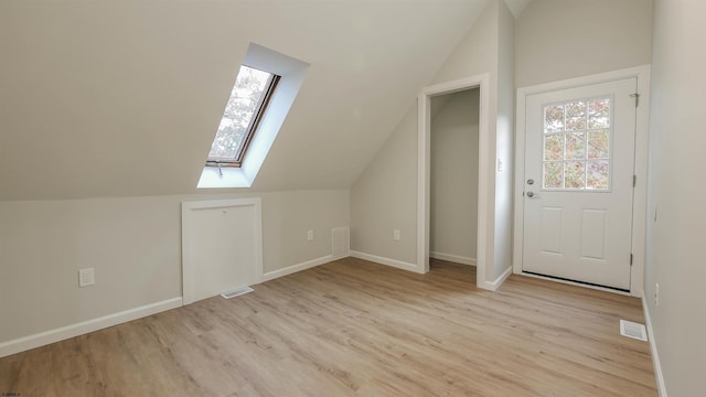 additional living space with vaulted ceiling with skylight and light hardwood / wood-style flooring