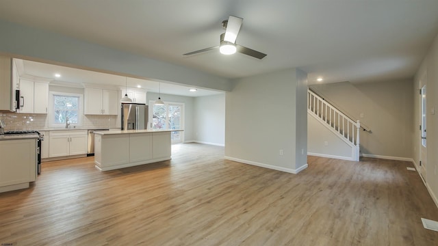 kitchen featuring a kitchen island, white cabinets, hanging light fixtures, stainless steel appliances, and light hardwood / wood-style flooring