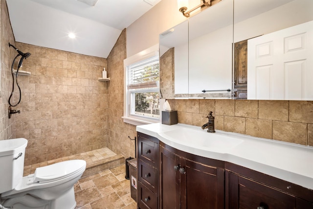 bathroom featuring toilet, tasteful backsplash, vaulted ceiling, a tile shower, and vanity