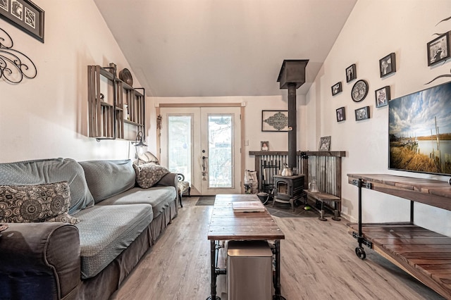 living room with wood-type flooring, vaulted ceiling, a wood stove, and french doors