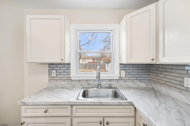 kitchen with light stone counters, sink, decorative backsplash, and white cabinets