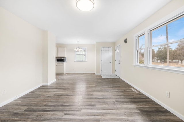 unfurnished living room with dark hardwood / wood-style floors, a wealth of natural light, and a notable chandelier