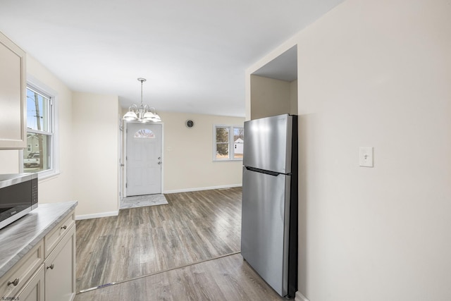 kitchen featuring stainless steel appliances, white cabinets, decorative light fixtures, a chandelier, and light wood-type flooring