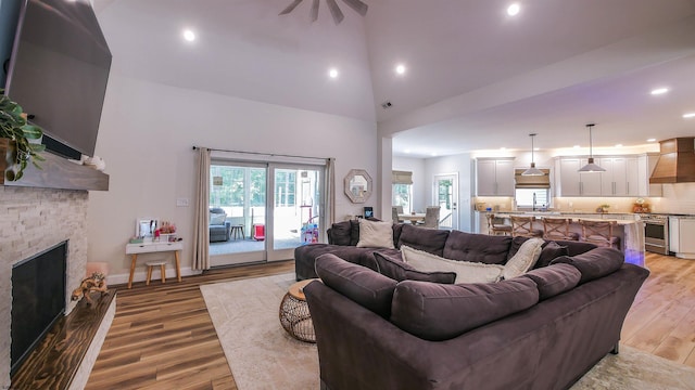 living room featuring sink, ceiling fan, a fireplace, light hardwood / wood-style floors, and a high ceiling