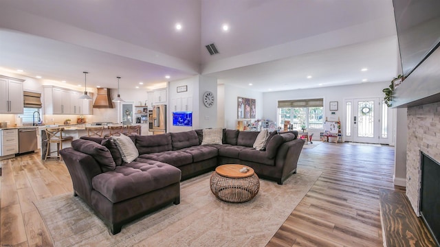 living room featuring a stone fireplace, a towering ceiling, sink, and light wood-type flooring