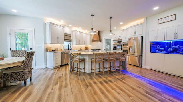 kitchen with appliances with stainless steel finishes, white cabinetry, hanging light fixtures, light stone countertops, and a kitchen island