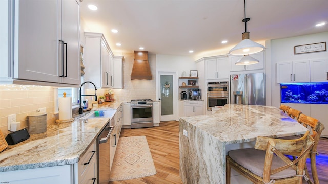 kitchen with appliances with stainless steel finishes, decorative light fixtures, white cabinetry, sink, and custom exhaust hood