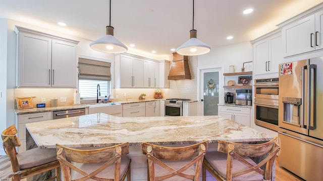 kitchen featuring wall chimney exhaust hood, high quality appliances, decorative light fixtures, and a breakfast bar