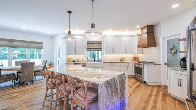 kitchen with pendant lighting, white cabinetry, custom range hood, and appliances with stainless steel finishes