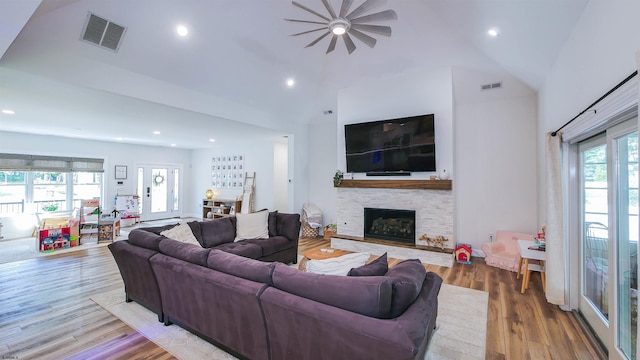 living room with a stone fireplace, hardwood / wood-style floors, and high vaulted ceiling