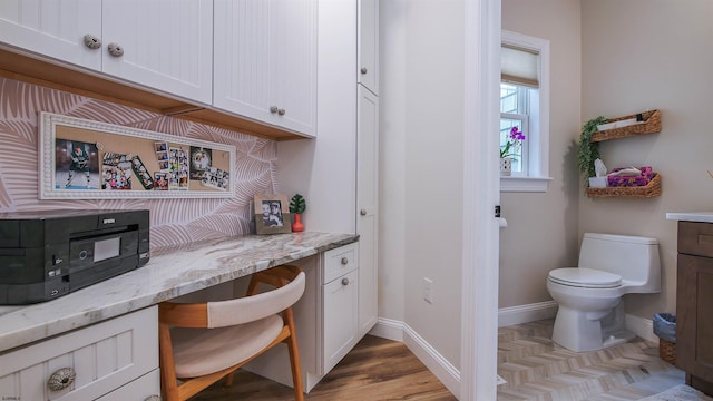 bar with white cabinetry, light stone counters, light hardwood / wood-style flooring, and built in desk