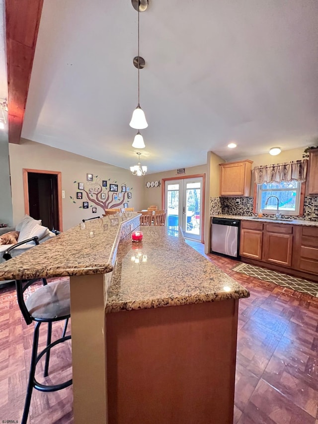 kitchen with pendant lighting, dishwasher, sink, a kitchen breakfast bar, and decorative backsplash