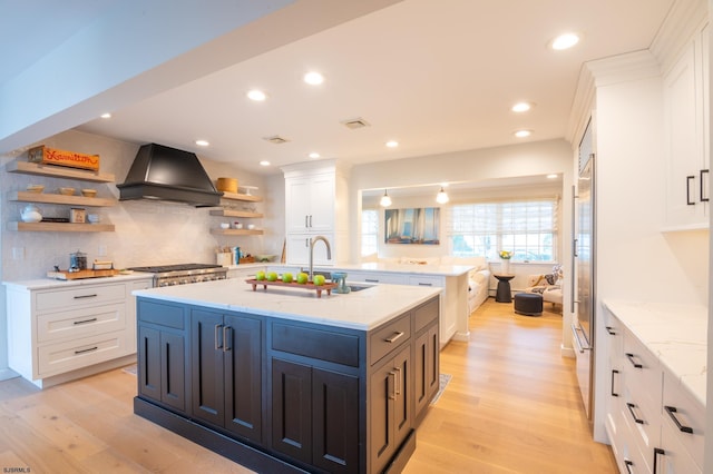 kitchen with appliances with stainless steel finishes, white cabinets, light stone counters, custom range hood, and light wood-type flooring