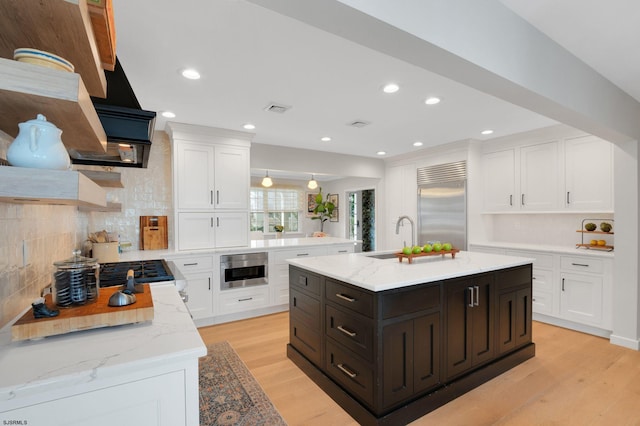 kitchen with stainless steel built in refrigerator, sink, a center island with sink, light hardwood / wood-style floors, and white cabinets