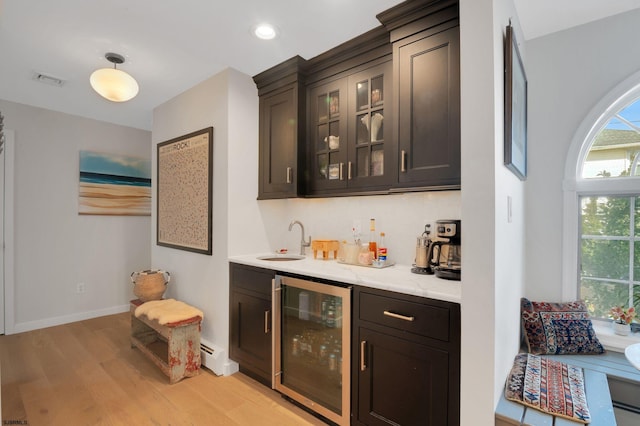 bar featuring dark brown cabinetry, beverage cooler, sink, and light wood-type flooring