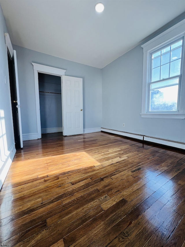 unfurnished bedroom featuring hardwood / wood-style flooring, a closet, and a baseboard heating unit