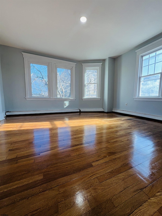 spare room featuring dark wood-type flooring, a baseboard radiator, and plenty of natural light