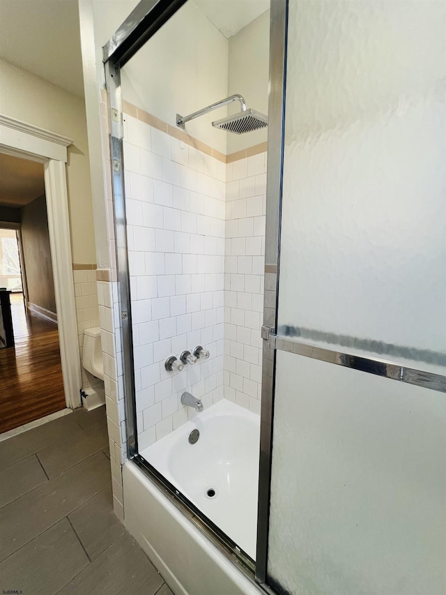 bathroom featuring enclosed tub / shower combo, toilet, and tile walls