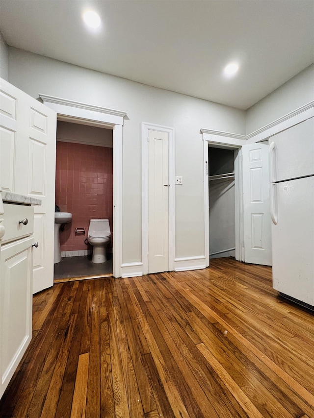 unfurnished bedroom featuring dark wood-type flooring, ensuite bathroom, and white refrigerator