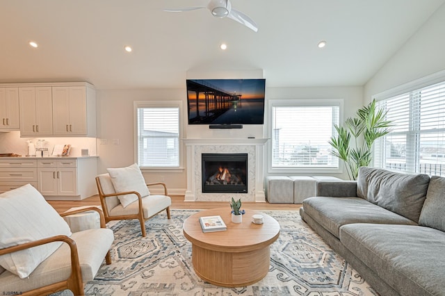 living room with ceiling fan, a fireplace, vaulted ceiling, and light hardwood / wood-style flooring