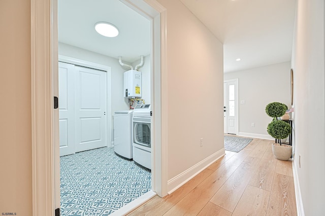 corridor with independent washer and dryer, tankless water heater, and light hardwood / wood-style floors