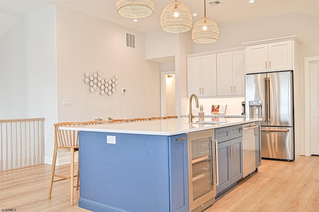 kitchen with sink, appliances with stainless steel finishes, white cabinets, decorative light fixtures, and beverage cooler