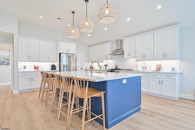 kitchen with high quality fridge, pendant lighting, white cabinets, and wall chimney exhaust hood