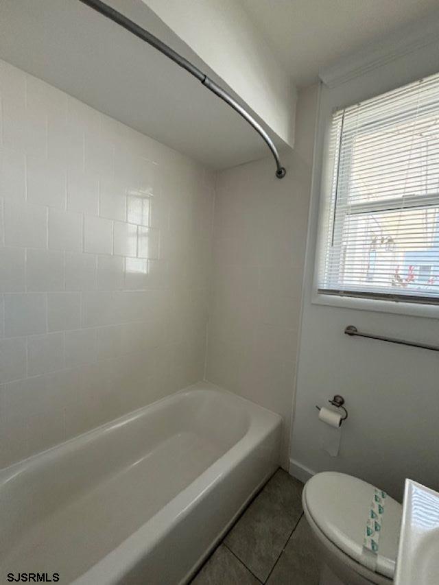 bathroom with baseboards, bathtub / shower combination, toilet, and tile patterned floors