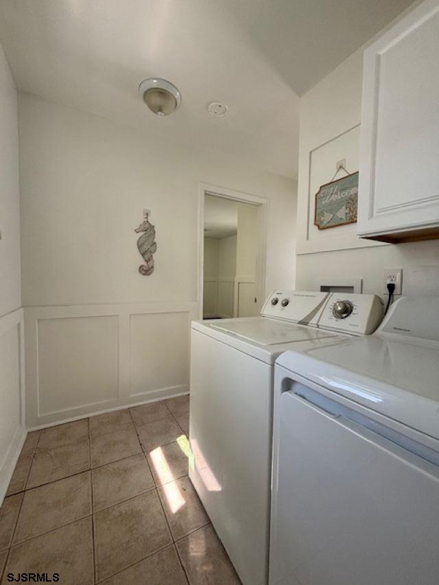 laundry room with light tile patterned floors, a decorative wall, wainscoting, cabinet space, and washing machine and clothes dryer