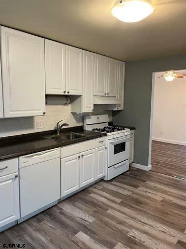 kitchen featuring dark wood finished floors, dark countertops, white cabinetry, a sink, and white appliances