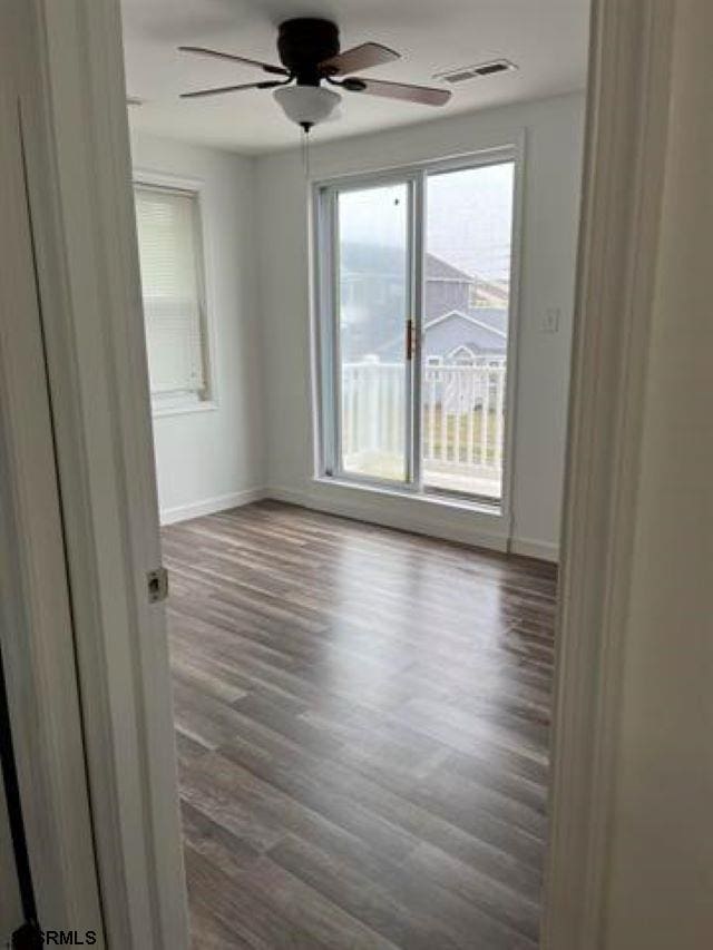 spare room featuring ceiling fan, baseboards, visible vents, and dark wood finished floors