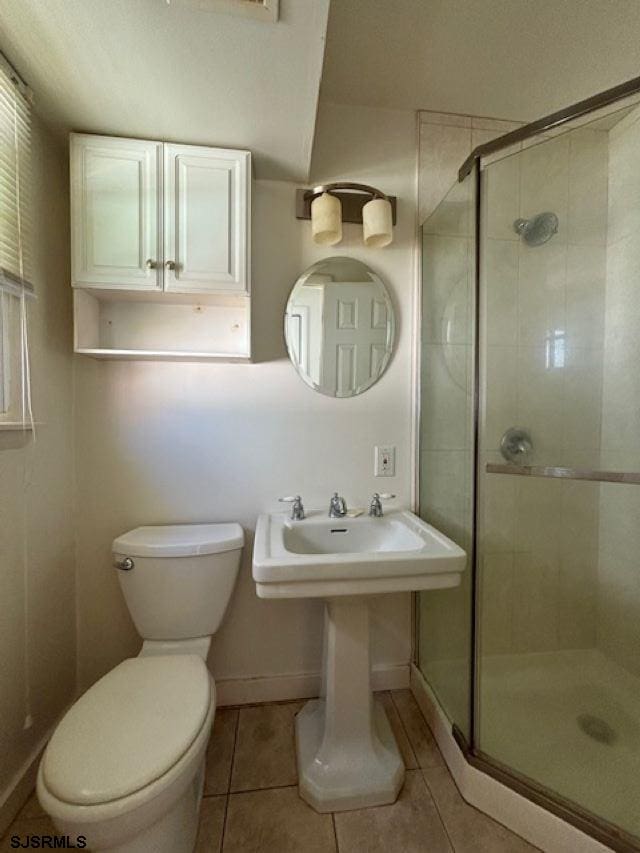 bathroom featuring a stall shower, baseboards, toilet, tile patterned floors, and a sink