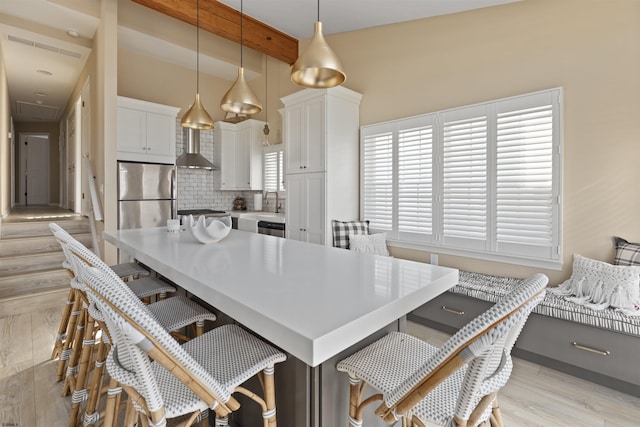 kitchen featuring a breakfast bar, white cabinetry, stainless steel fridge, hanging light fixtures, and a center island