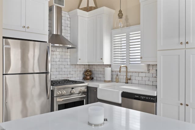 kitchen with appliances with stainless steel finishes, tasteful backsplash, white cabinetry, hanging light fixtures, and wall chimney exhaust hood