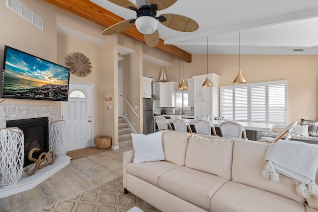 living room featuring beam ceiling, high vaulted ceiling, light wood-type flooring, ceiling fan, and a premium fireplace