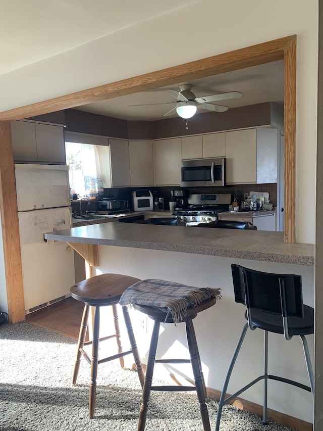 kitchen featuring tasteful backsplash, appliances with stainless steel finishes, a kitchen breakfast bar, and kitchen peninsula