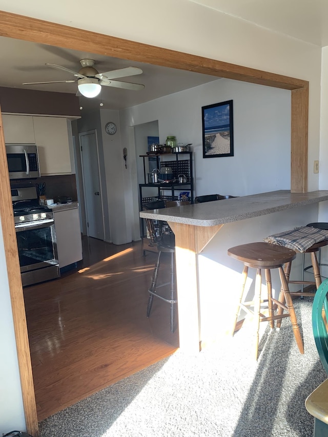 kitchen featuring a breakfast bar, ceiling fan, white cabinetry, stainless steel appliances, and dark hardwood / wood-style flooring