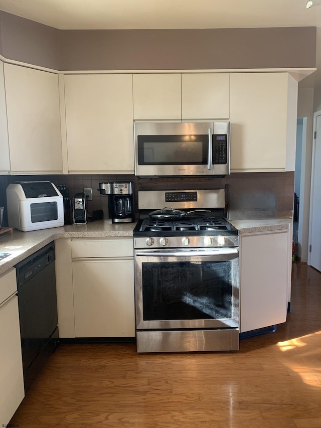 kitchen with tasteful backsplash, hardwood / wood-style floors, white cabinets, and appliances with stainless steel finishes