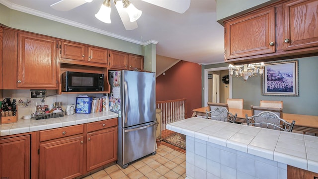 kitchen with light tile patterned flooring, crown molding, tile counters, stainless steel fridge, and ceiling fan