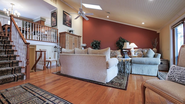 living room featuring lofted ceiling with skylight, wood-type flooring, ornamental molding, and ceiling fan with notable chandelier