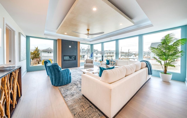 living room featuring a large fireplace, light hardwood / wood-style floors, a raised ceiling, and a healthy amount of sunlight