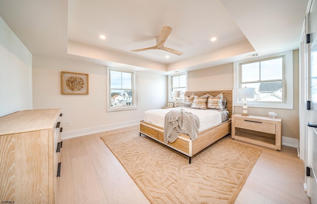 bedroom featuring a tray ceiling, ceiling fan, and light wood-type flooring