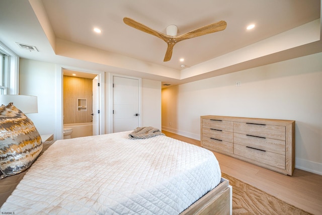 bedroom with light hardwood / wood-style flooring, a raised ceiling, ceiling fan, and ensuite bathroom