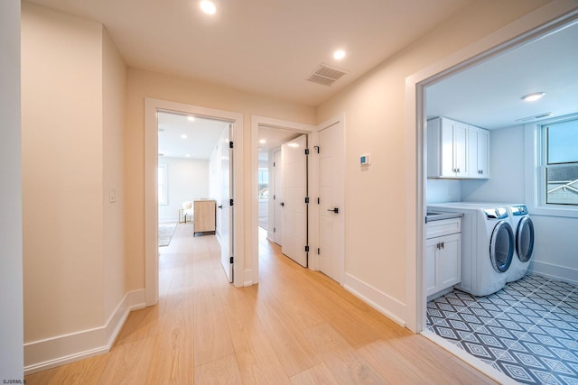 clothes washing area with washer and dryer, light hardwood / wood-style flooring, and cabinets