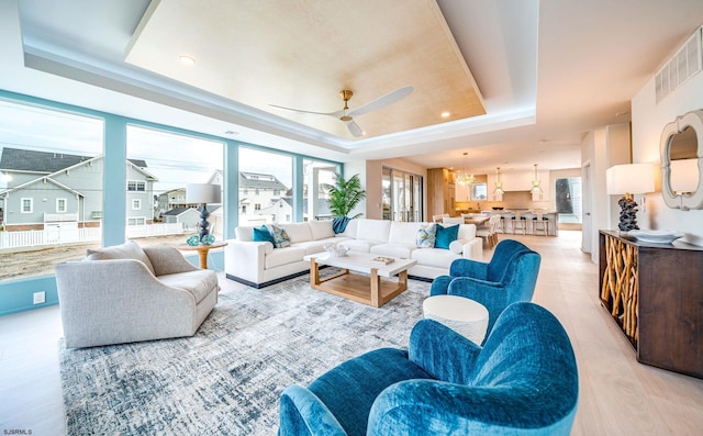 living room featuring light wood-type flooring, ceiling fan, and a tray ceiling