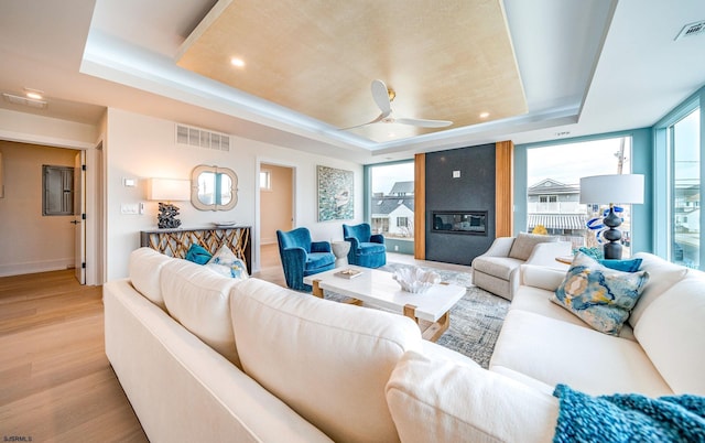 living room featuring a raised ceiling, ceiling fan, a fireplace, and light hardwood / wood-style floors