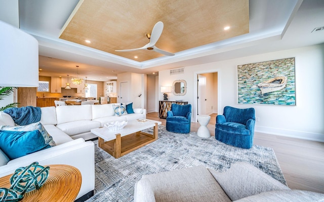 living room with wood-type flooring, a raised ceiling, and ceiling fan