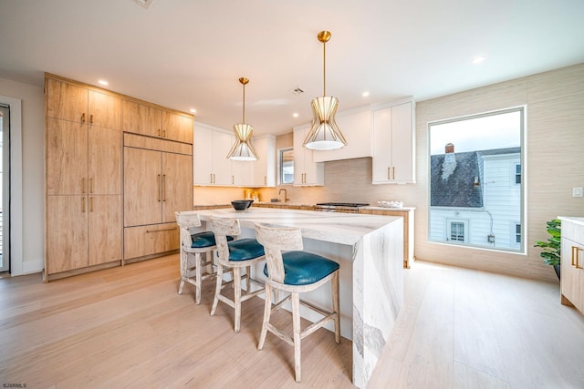 kitchen with a breakfast bar area, white cabinetry, decorative light fixtures, paneled built in fridge, and a kitchen island